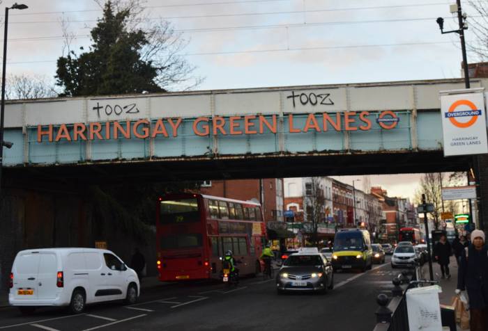 A view of Green Lanes in London Harringay with a train bridge in the foreground that reads: Harringay Green Lanes