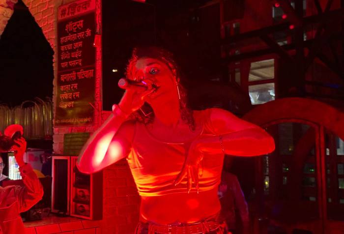 A close-up shot of Delhi hip-hop artists Kinari performing on stage. They are wearing a cropped top, holding the mic in the right hand and drenched in red light.