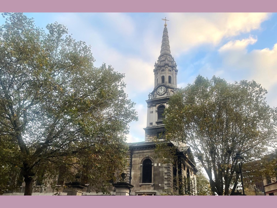 St Giles-in-the-Fields church in London, the spire looming into the sky behind two trees in the foreground