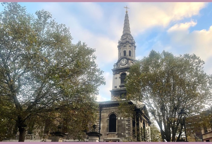 St Giles-in-the-Fields church in London, the spire looming into the sky behind two trees in the foreground