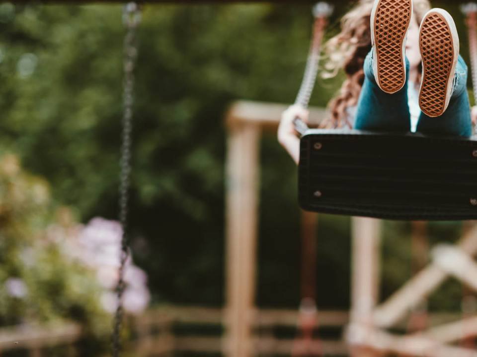 A child on a swing, swinging high and we mainly see her shoes from below.