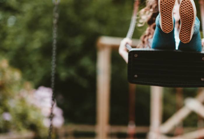 A child on a swing, swinging high and we mainly see her shoes from below.